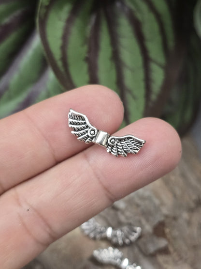 Eine kleine Feder-Engelsflügel-Zwischenperle in Antik-Silber auf einer Fingerkuppe präsentiert als Größenvergleich.