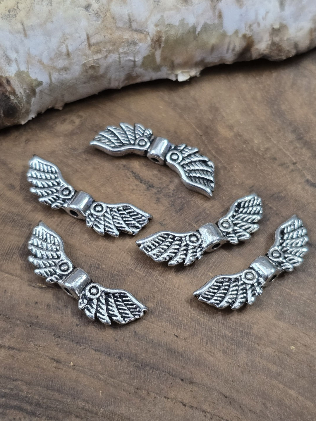 Fünf silberne Flügel-Zwischenperlen mit Federmuster (22 mm) flach liegend zur Ansicht der Bohrung und Rückseite.