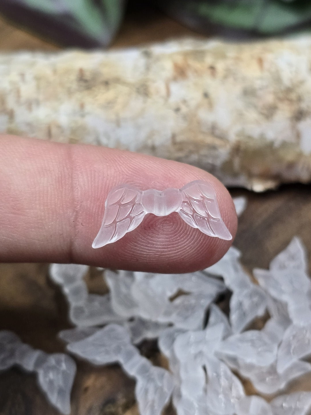 Kleine gefrostete Engelsflügel-Perle in Weiß auf einer Fingerspitze als Größenvergleich.