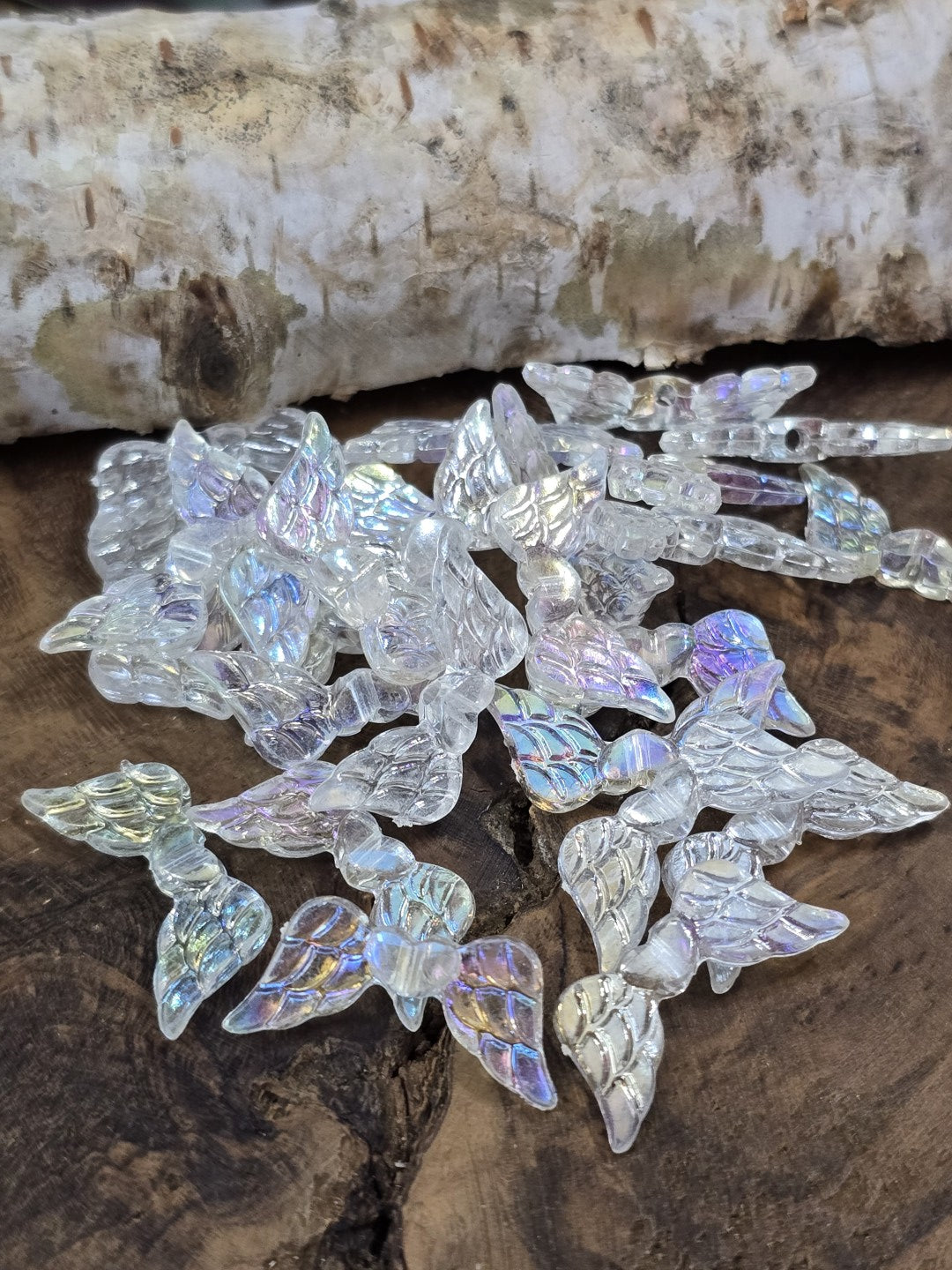 Transparente Engelsflügel-Perlen mit Regenbogen-Schimmer (AB-Effekt) auf Holzuntergrund.