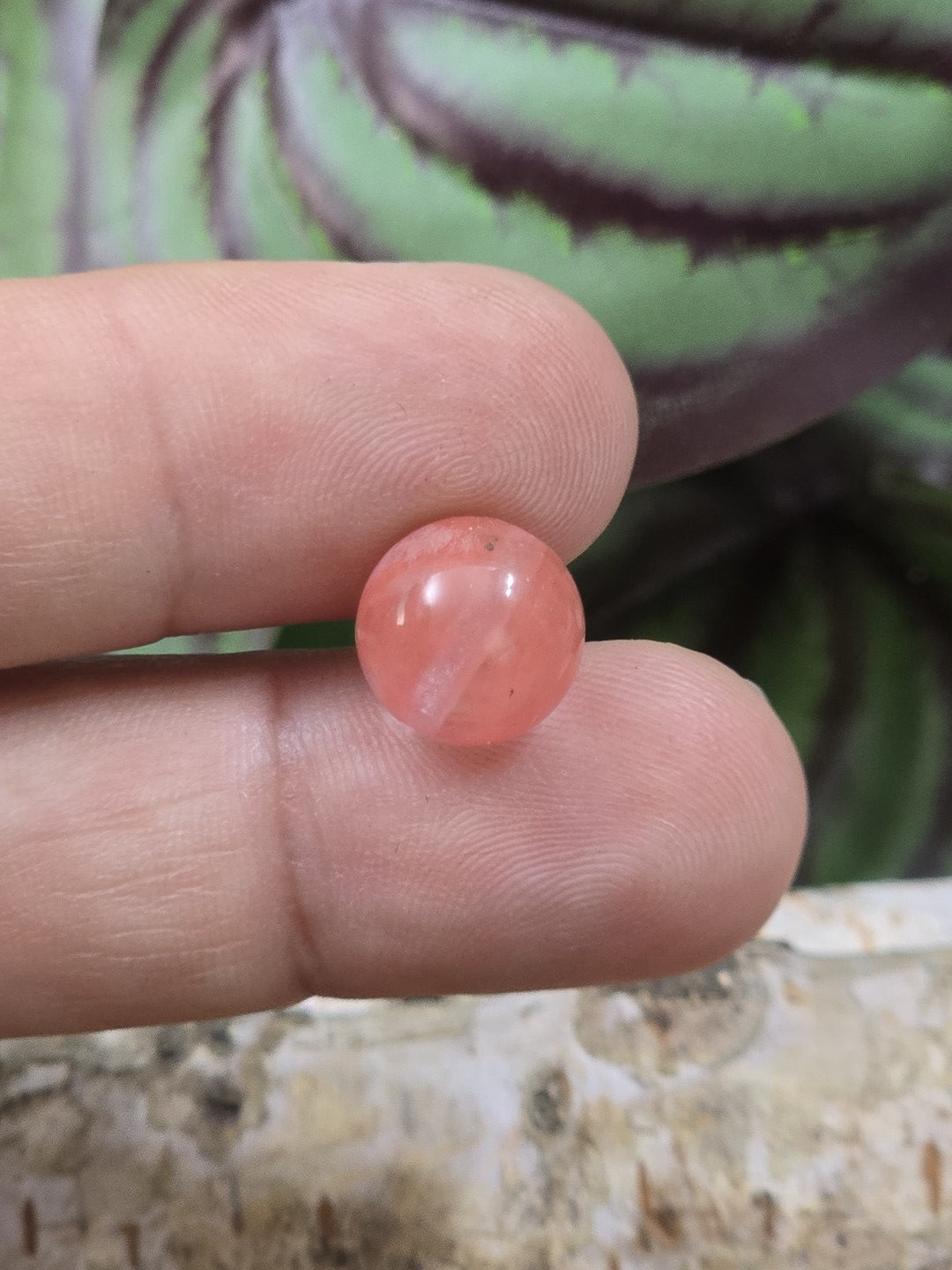Rote Erdbeerquarz-Perle mit 10 mm Durchmesser auf den Fingern als Größenvergleich
