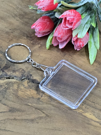 Transparenter quadratischer Acryl-Schlüsselanhänger zum Befüllen mit eigenem Foto vor rosa Tulpen auf Holzgrund.