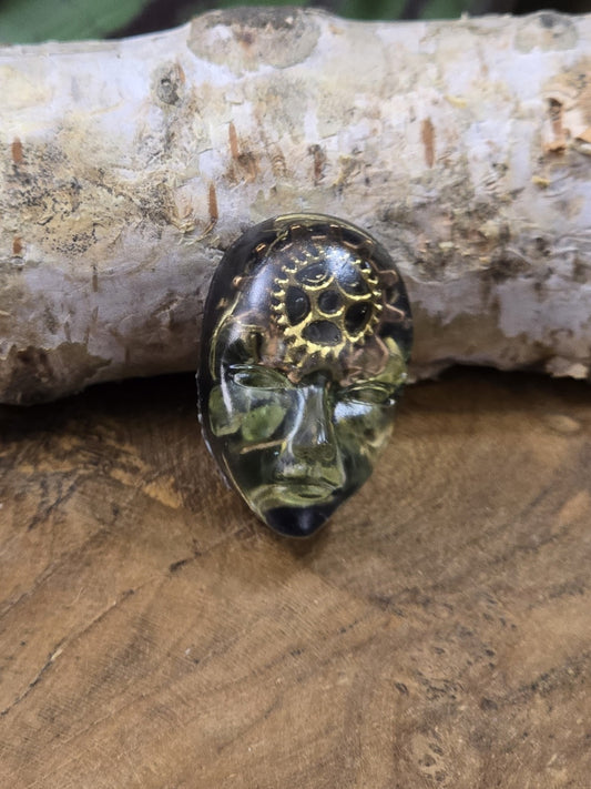 Dunkelgrüner Resin-Cabochon mit Gesichtsmotiv, Zahnrädern und goldfarbenen Steampunk-Details