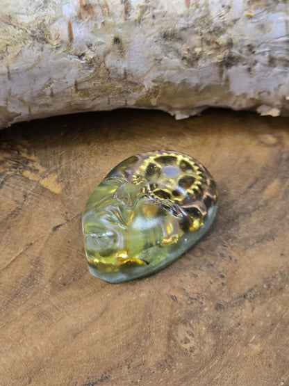 Liegender grüner Resin-Cabochon mit Gesichtsrelief und metallischen Zahnrädern für Schmuckdesign