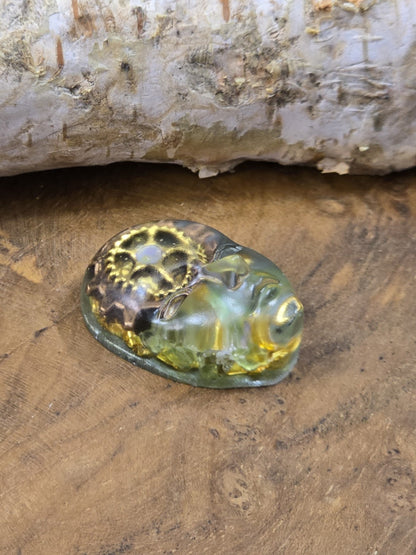 Seitliche Ansicht eines grün-transparenten Gesicht-Cabochons mit Steampunk-Elementen auf Holz