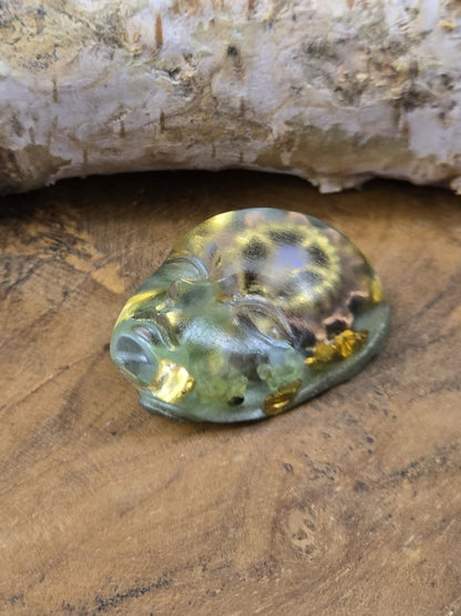 Seitlich liegender Resin-Cabochon mit Gesichtsrelief, grün-goldener Optik und Steampunk-Elementen