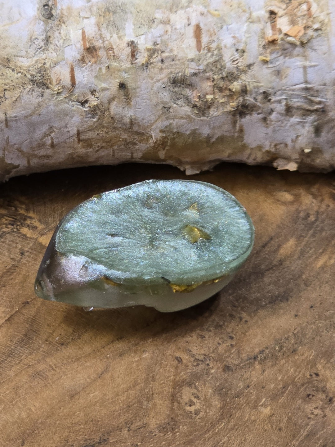Rückseite eines großen grünen Resin-Cabochons mit flacher Form und sichtbaren goldfarbenen Einschlüssen