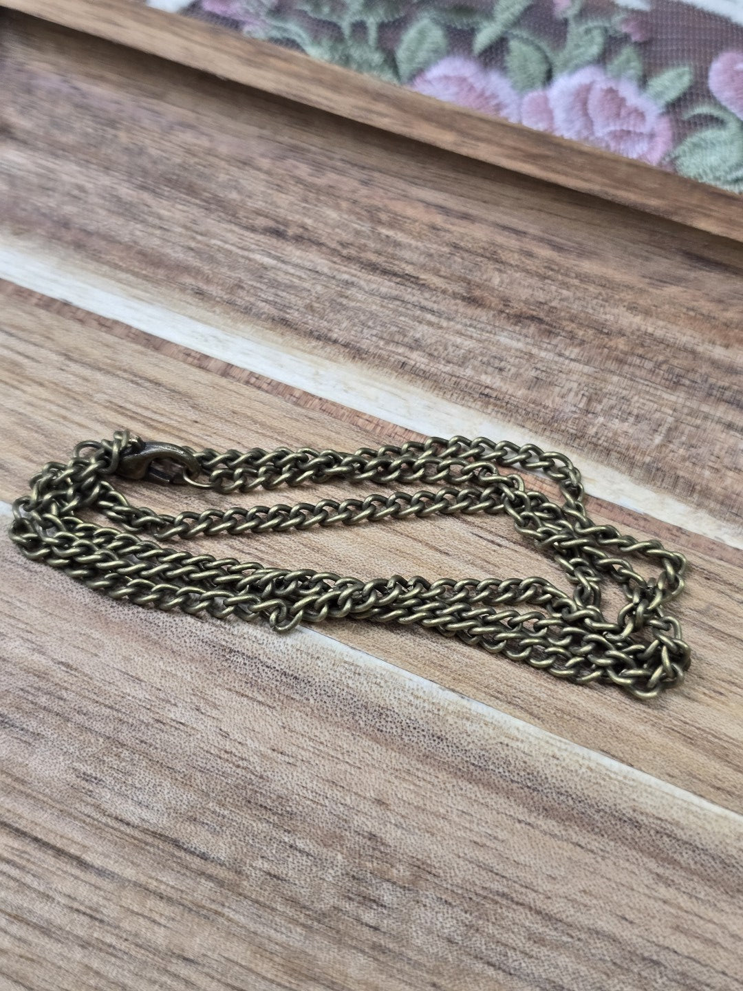Zusammengelegte Bronze-Gliederkette mit Karabinerverschluss auf Holzuntergrund.