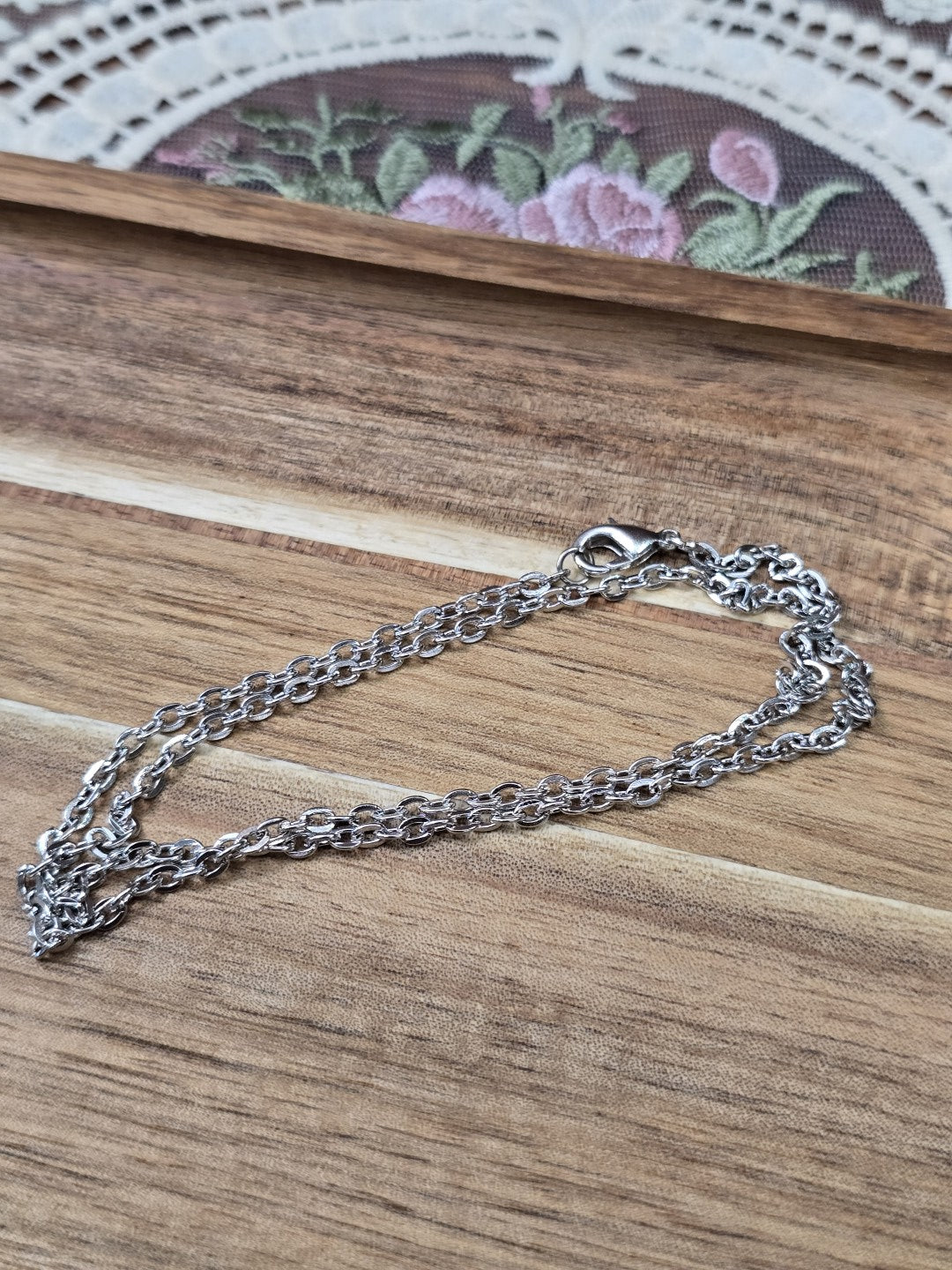 Zusammengelegte dunkelsilberne Gliederkette mit Karabinerverschluss auf Holzuntergrund.