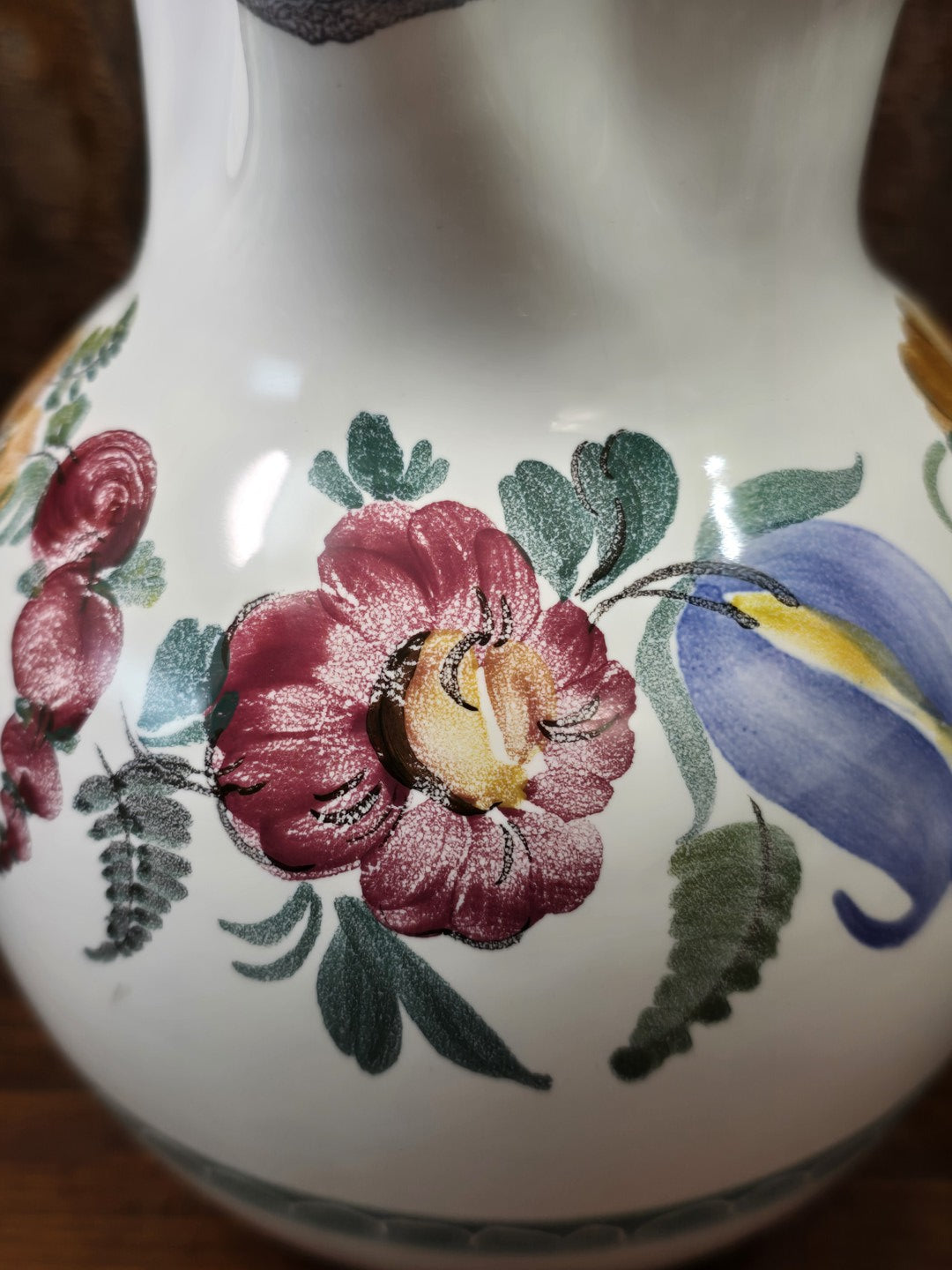 Vintage Keramikkrug mit floralem Dekor aus roter Blüte, blauem Blütenmotiv und grünen Blättern in einer Nahaufnahme.