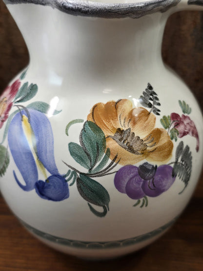 Vintage Keramikkrug mit ockerfarbener und violetter Blüte, blauem Blütenmotiv sowie grünen Blättern in detaillierter Nahansicht.