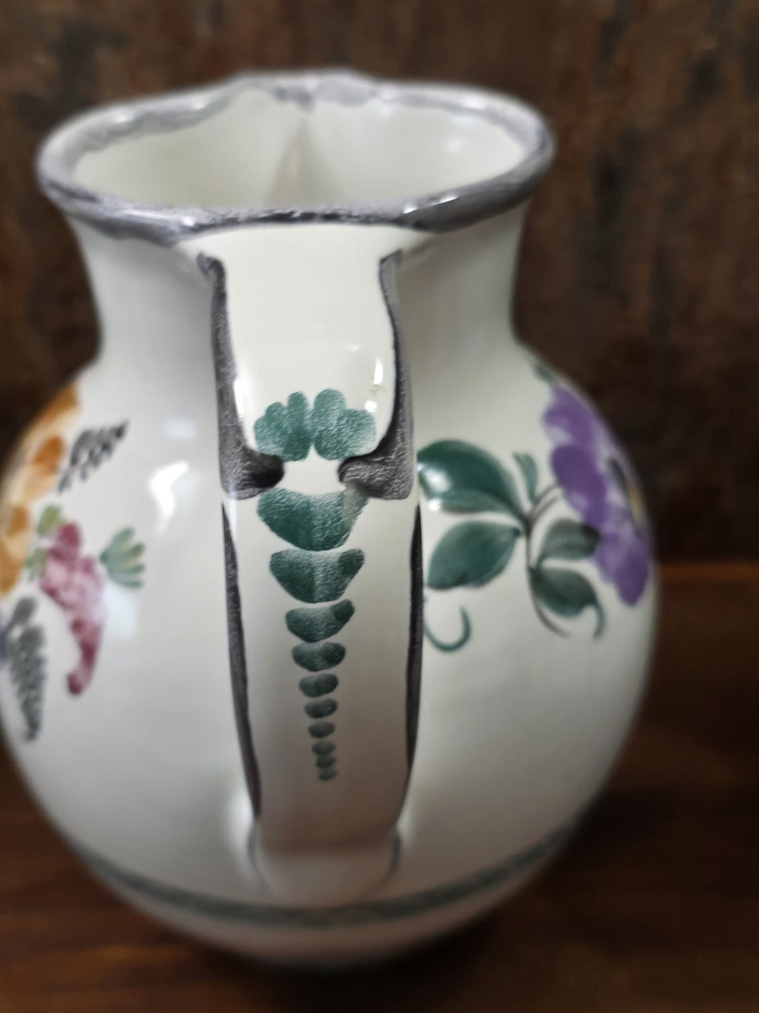 Vintage Keramikkrug mit breitem Henkel, grünem Blattmotiv und floralem Dekor an den Seiten, von der Rückseite fotografiert.