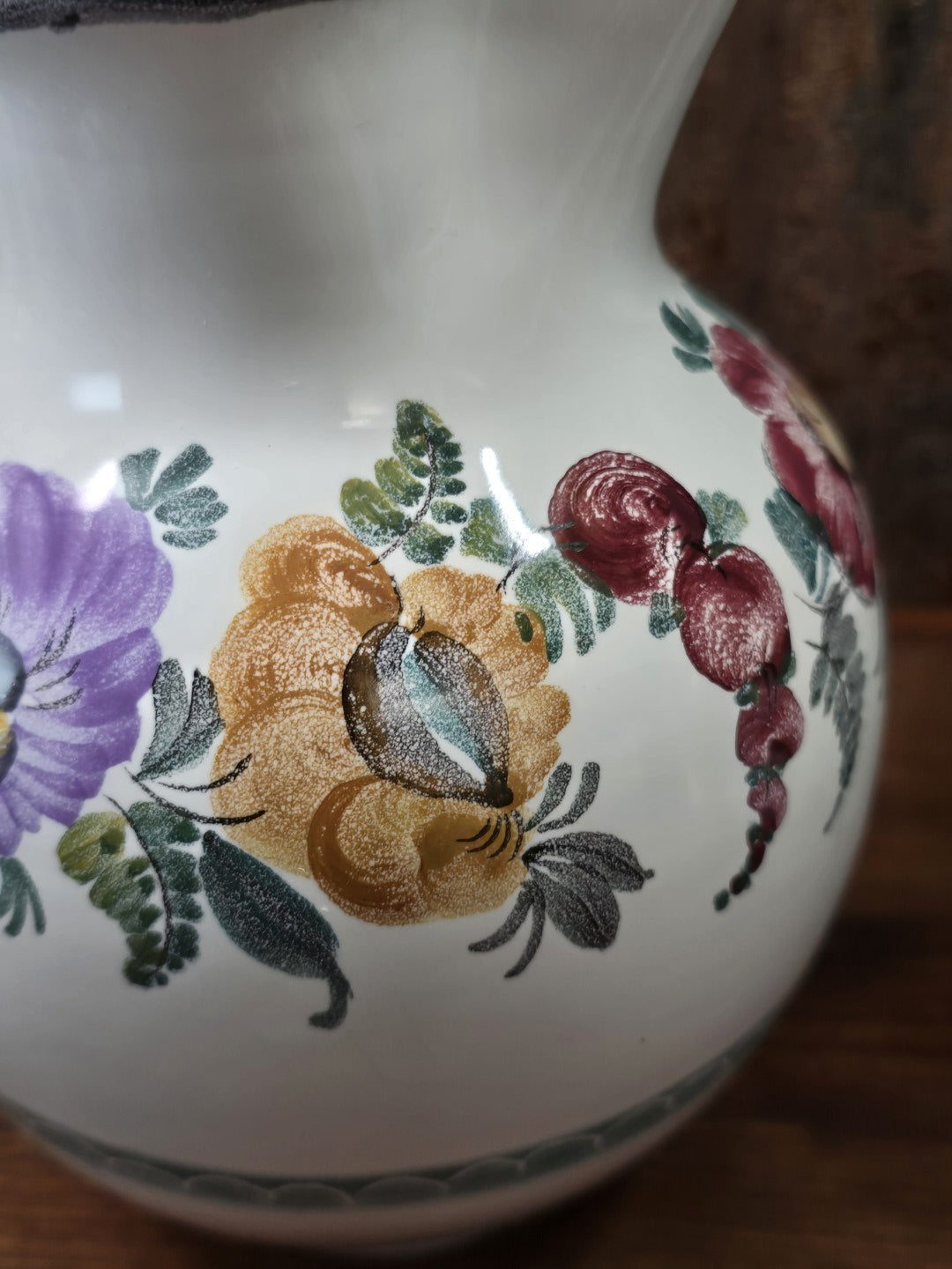 Vintage Keramikkrug mit ockerfarbener Blüte, roten Blütenformen und grünen Blättern, florales Dekor in Nahaufnahme.
