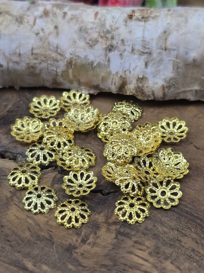 Filigrane Perlenkappen in Gold mit blütenförmigem Muster zur Schmuckherstellung ausgelegt auf Holz.