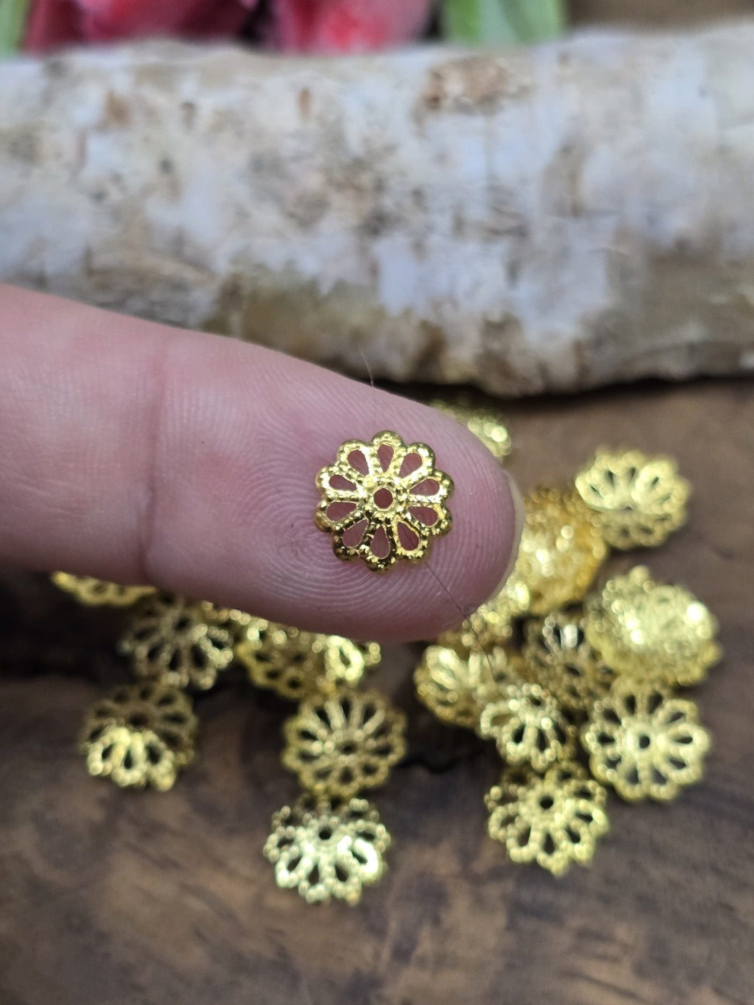 Kleine goldene Perlenkappe in Blütenform auf einer Fingerspitze zur Größenveranschaulichung.
