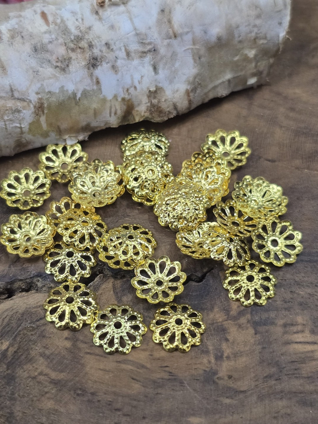 Mehrere goldfarbene Schmuck-Perlenkappen aus Metall mit gestanztem Blumenmuster im Detail.