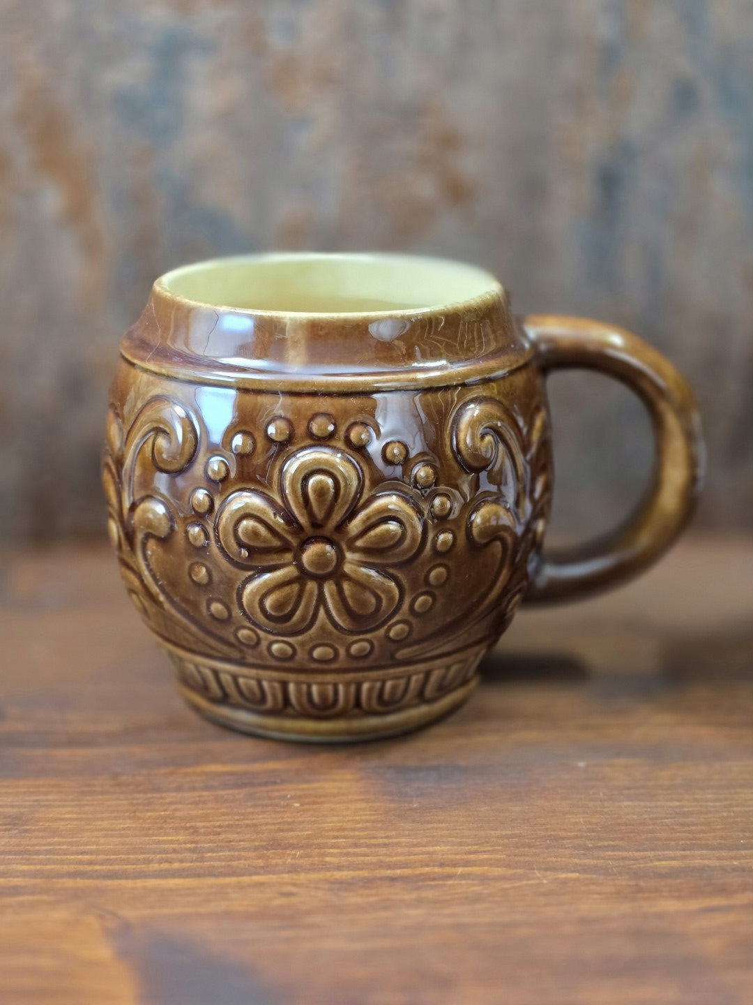 Vintage Keramikbecher von Gräfenroda mit glänzender brauner Glasur, großem Blumenrelief und rundem Henkel auf Holztisch