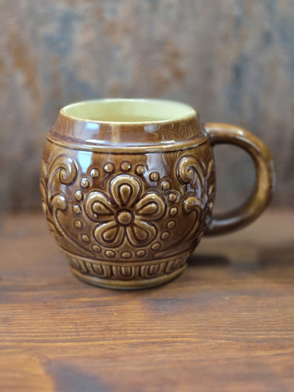 Vintage Keramikbecher von Gräfenroda mit glänzender brauner Glasur, großem Blumenrelief und rundem Henkel auf Holztisch