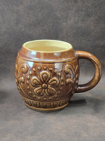 Vintage Keramikbecher mit brauner Glasur, floralem Reliefmuster und hellem Innenbereich in klarer Frontalansicht auf dunklem Hintergrund