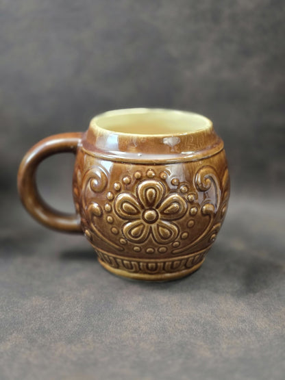 Vintage Keramikbecher mit brauner Glasur, symmetrischem Blumenrelief und seitlichem Henkel in gedrehter Ansicht auf dunklem Hintergrund