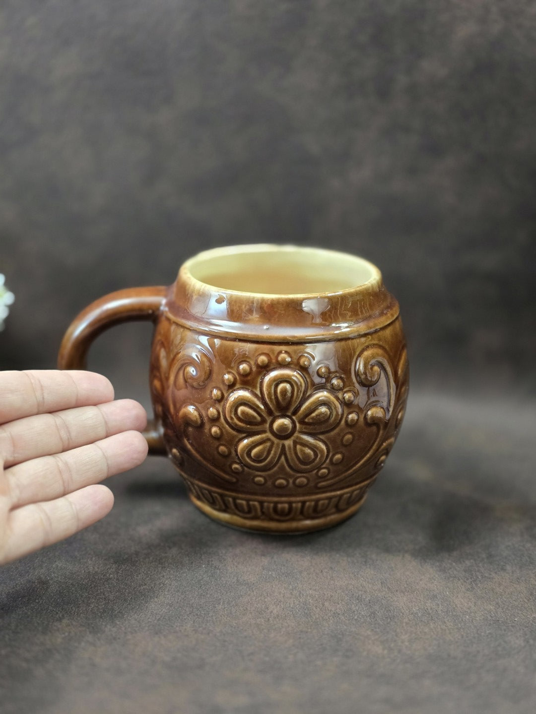 Vintage Keramikbecher von Gräfenroda mit floralem Reliefdekor und brauner Glasur neben einer Hand als Größenvergleich