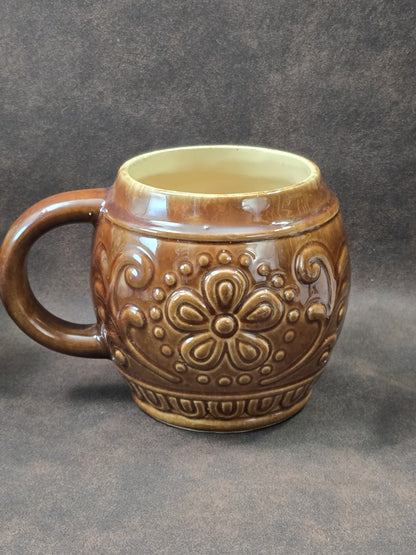 Vintage Keramikbecher mit brauner Hochglanzglasur, großem Blumenmotiv und ornamentiertem Reliefband in detaillierter Nahaufnahme