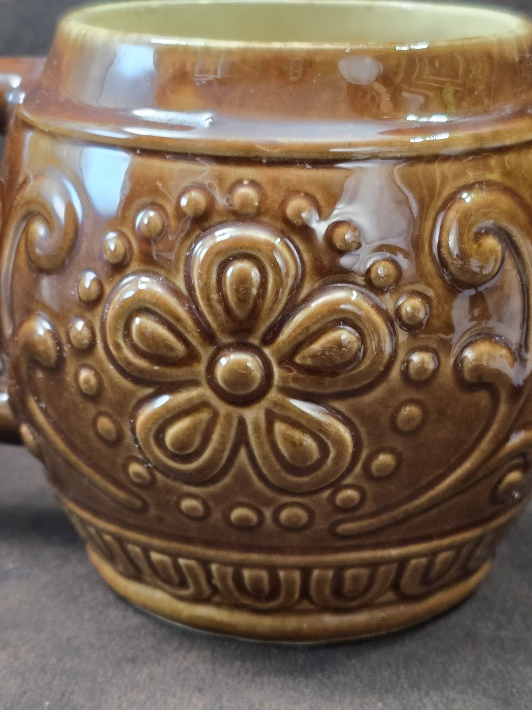 Vintage Keramikbecher mit kräftigem rundem Henkel, brauner Glasur und reliefiertem Dekor in seitlicher Detailansicht