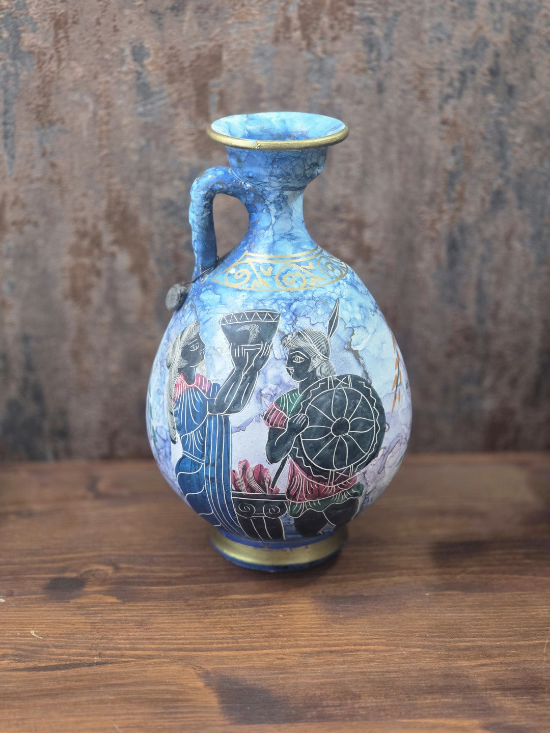 Vintage Keramikkanne in Blau mit Golddekor und zwei schwarz konturierten Figuren mit Gefäß und Rundschild in Rückansicht