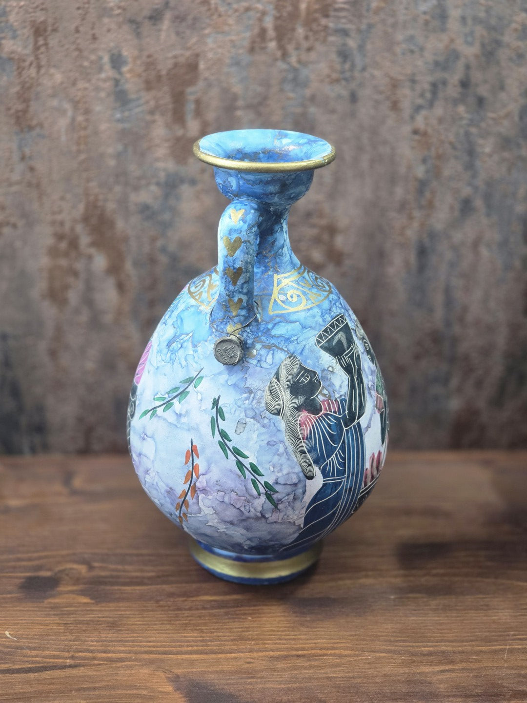 Vintage Keramikkanne mit blauem Henkel, goldfarbenen Herzdetails und Figurenmotiv, schräg von hinten auf Holztisch fotografiert