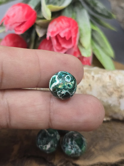 Eine grüne 12 mm Mosaik-Steinperle zwischen den Fingern gehalten als Größenvergleich für die Schmuckherstellung.