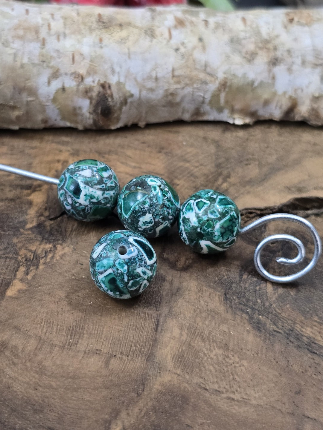 Drei grüne Mosaik-Steinperlen (12 mm) auf einen Metalldraht aufgefädelt mit einer davor liegenden Perle.