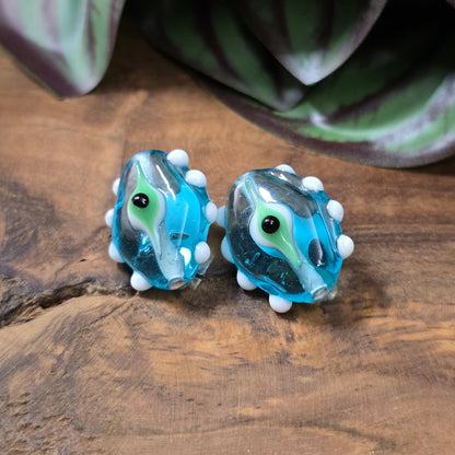 2 handgefertigte Lampwork-Glasperlen in Blau, Oval mit Noppen & Augenmotiv. Einzigartiges Material für kreative Schmuckherstellung.