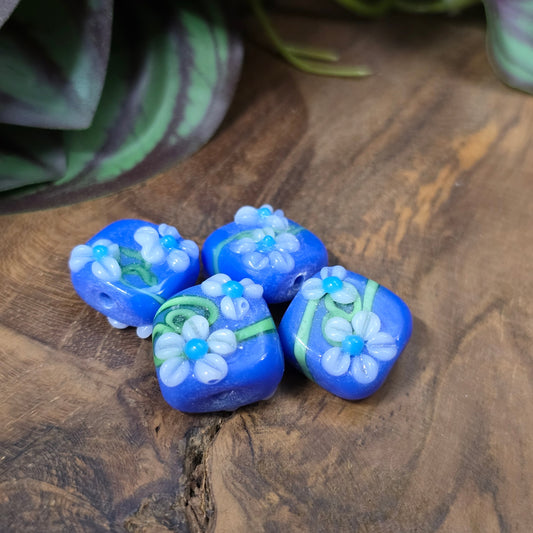 4 handgefertigte Lampwork-Glasperlen, quadratisch in Blau mit Blütendekor. Hochwertiges Material für individuelle Schmuckherstellung.
