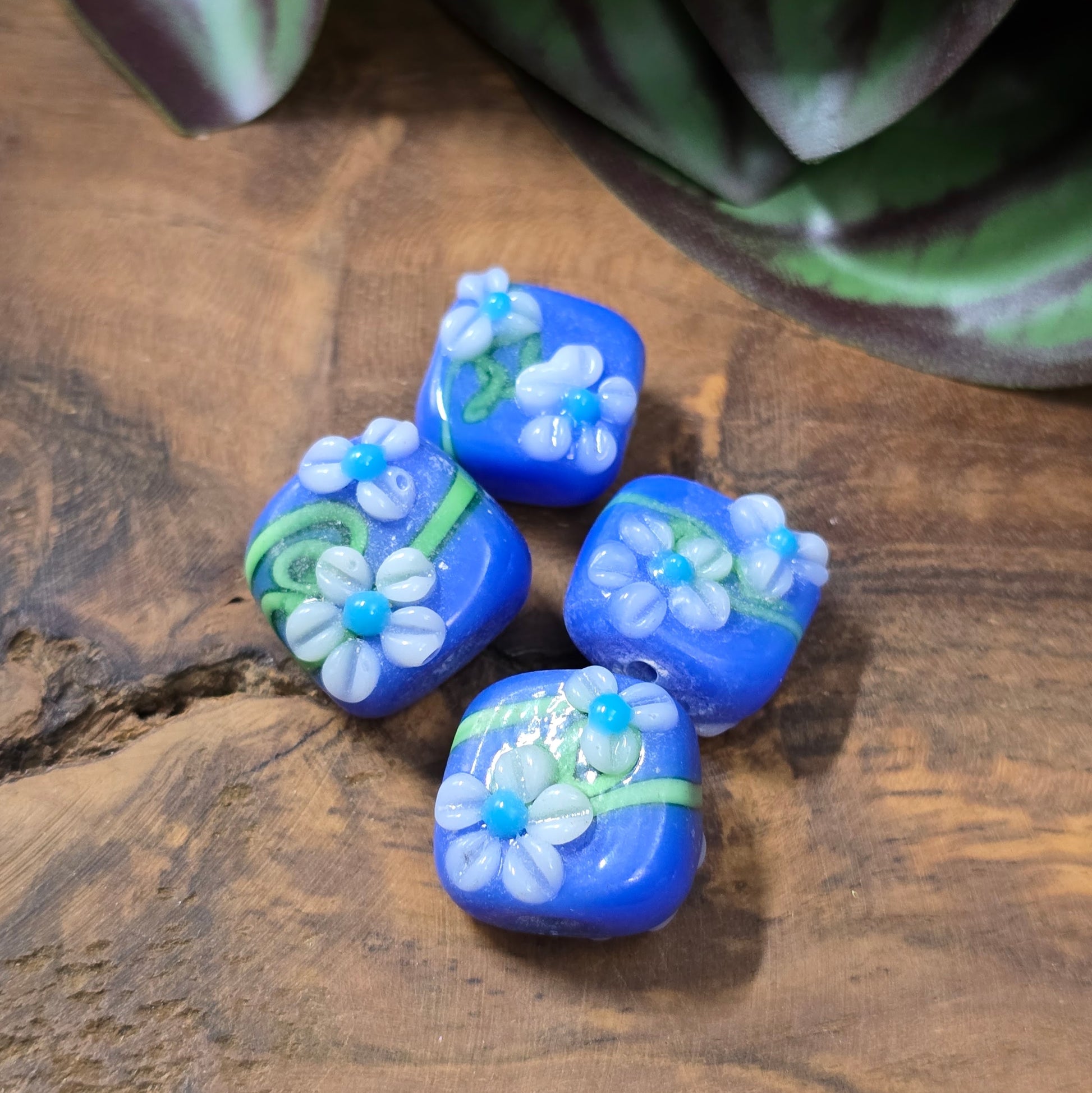 4 handgefertigte Lampwork-Glasperlen, quadratisch in Blau mit Blütendekor. Hochwertiges Material für individuelle Schmuckherstellung.