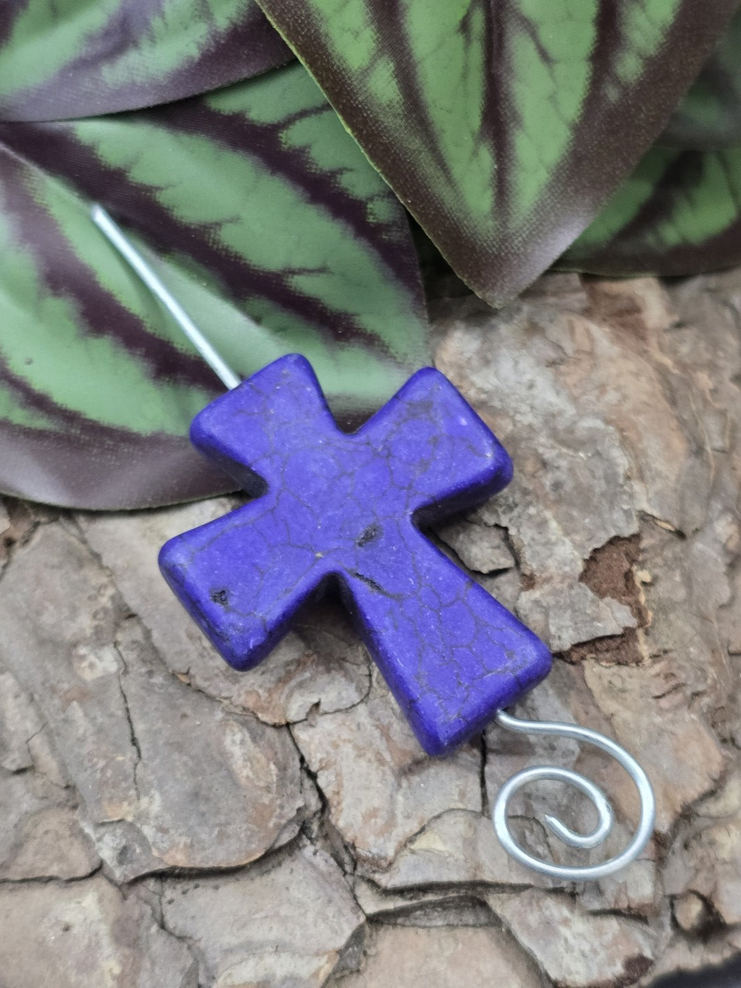 Lila Howlith Kreuzperle mit durchgefädeltem Silberdraht auf Baumrinde zur Demonstration der Bohrung