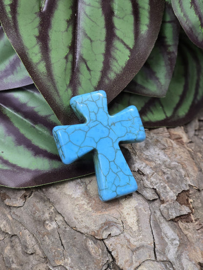 Schräg liegende Howlith Kreuzperle in Türkis auf rustikalem Holzgrund für DIY-Schmuck