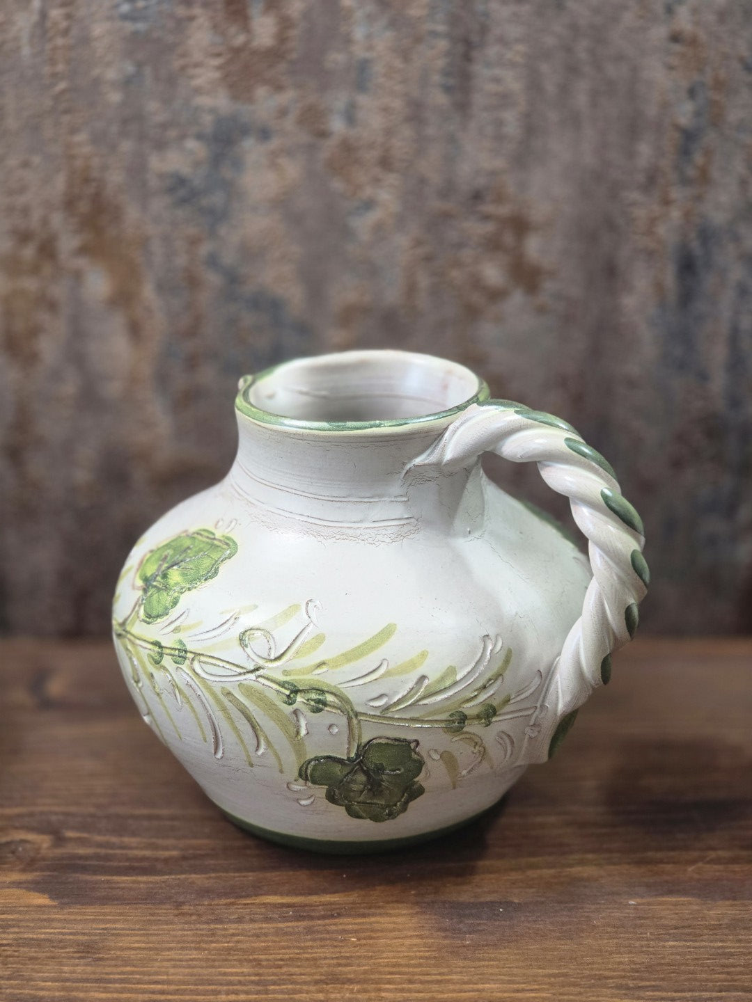 Vintage Keramikkrug mit rundem Korpus, floraler Verzierung in Grün und hellem gedrehtem Henkel von der Rückseite fotografiert