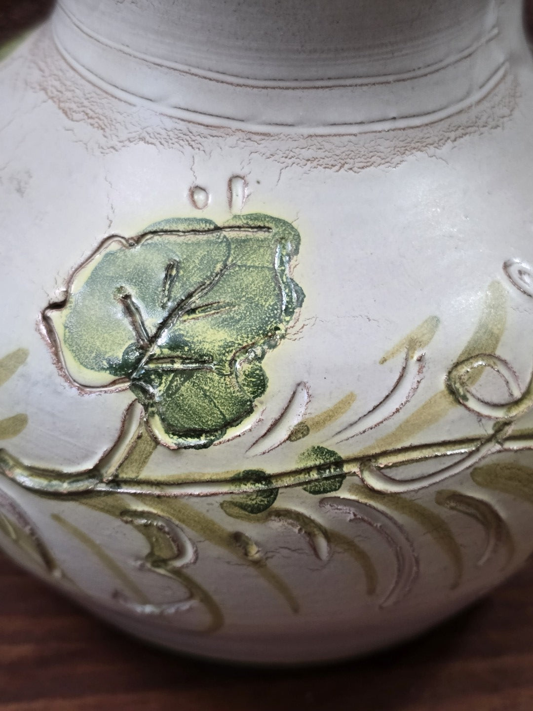 Vintage Keramikkrug mit plastischem grünem Blatt- und Rankendekor auf cremefarbenem Grund in detaillierter Nahaufnahme