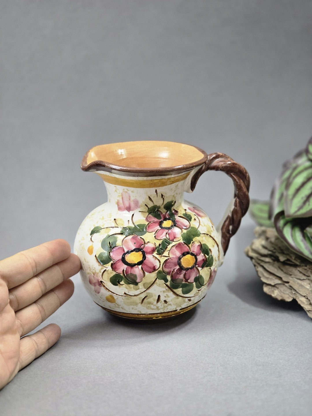 Vintage Henkelkrug aus Keramik mit floraler Bemalung, Sgraffito-Details, cremefarbener Glasur und Größenvergleich mit Hand