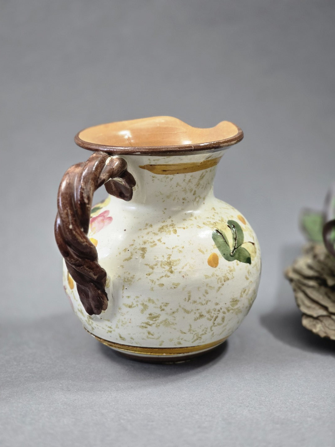 Rückseite des Vintage Blumenkrugs mit hellem Keramikkörper, braunem Henkel, gesprenkelter Oberfläche und gewelltem Ausguss