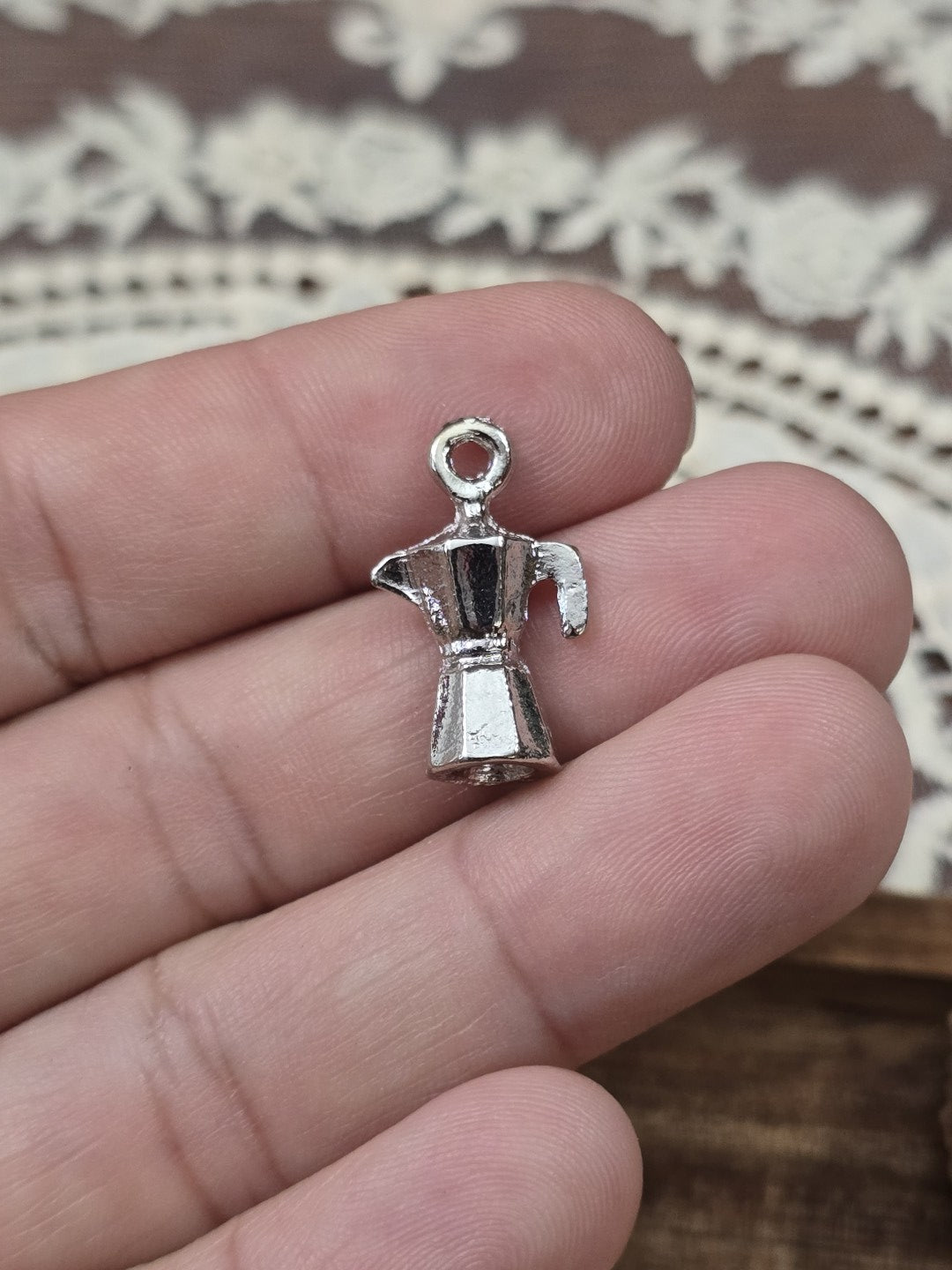Kaffeekocher-Schmuckanhänger 21mm in Silber-Optik quer auf den Fingern gehalten als Größenvergleich.