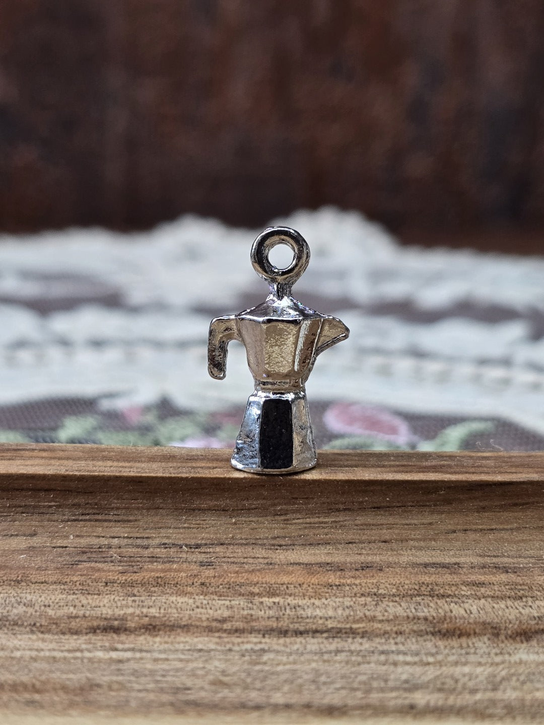 Kaffeekocher-Schmuckanhänger in Silber-Optik aufrecht stehend auf Holzgrund.