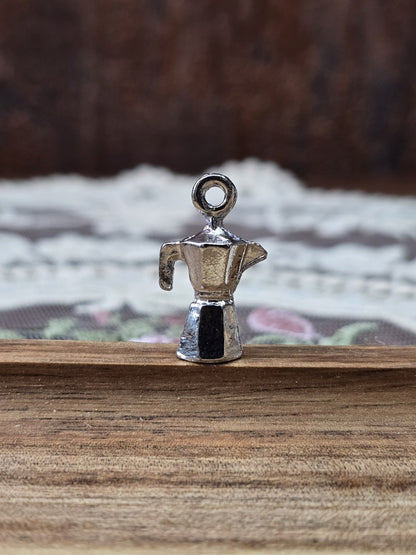 Kaffeekocher-Schmuckanhänger in Silber-Optik aufrecht stehend auf Holzgrund.