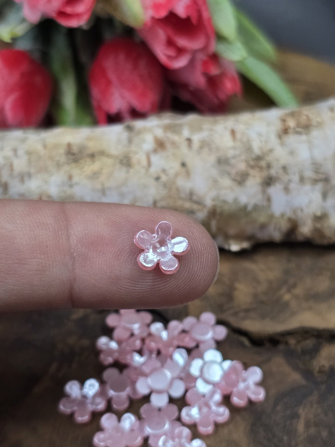 Eine winzige rosafarbene Kunststoff-Blüte auf einer Fingerkuppe präsentiert zum praktischen Größenvergleich für filigrane Bastelarbeiten.