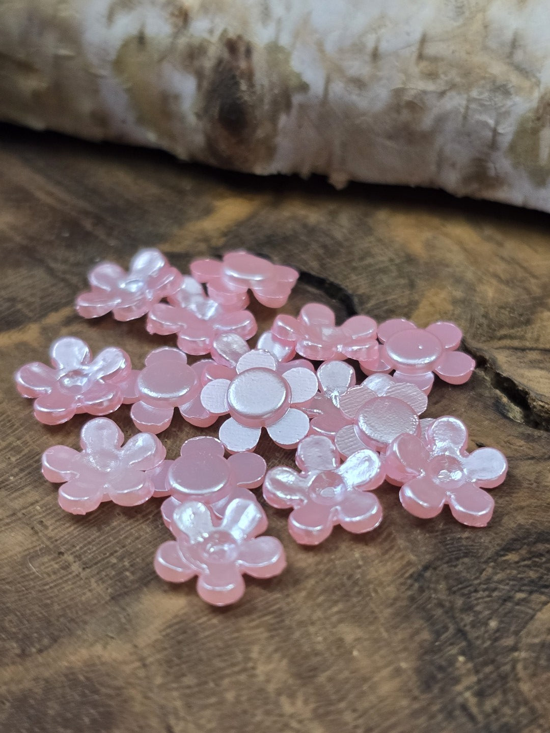 Detailansicht der glänzenden Mini-Blumen in Hellrosa, dekoriert auf dunklem Echtholz vor einem hellen Birkenstamm.