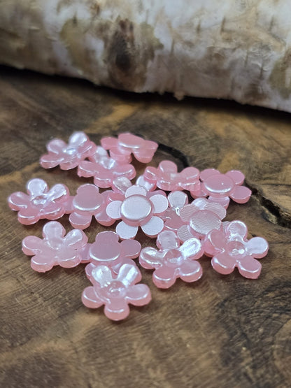 Detailansicht der glänzenden Mini-Blumen in Hellrosa, dekoriert auf dunklem Echtholz vor einem hellen Birkenstamm.