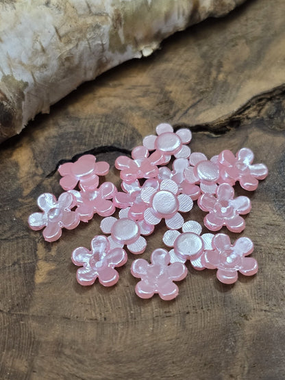 Mehrere 8 mm Cabochon-Blüten in Rosa zum Aufkleben, teils mit der flachen Unterseite nach oben zeigend zur Ansicht der Klebefläche.