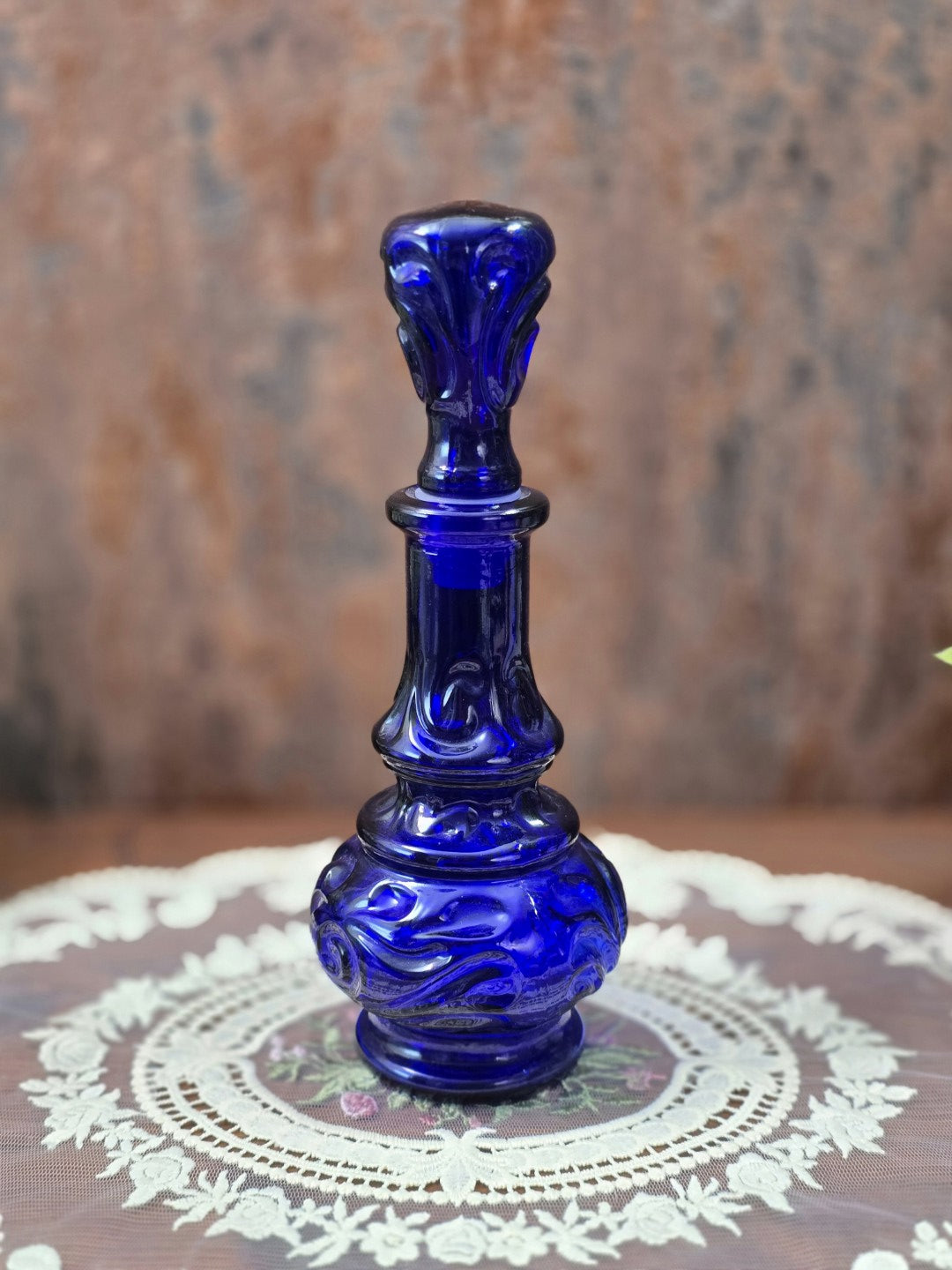 Vintage Glasflakon in Kobaltblau mit langem Hals, reliefiertem Ornamentdekor und passendem Glasstopfen auf dekorativer Spitzendecke