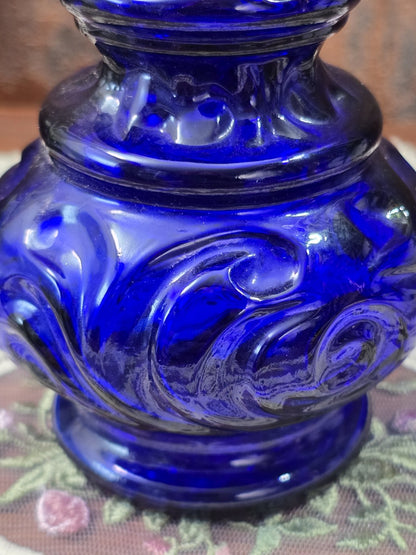 Vintage Glasflakon aus kobaltblauem Glas mit plastischen geschwungenen Ornamenten am bauchigen Flaschenkörper in Nahaufnahme