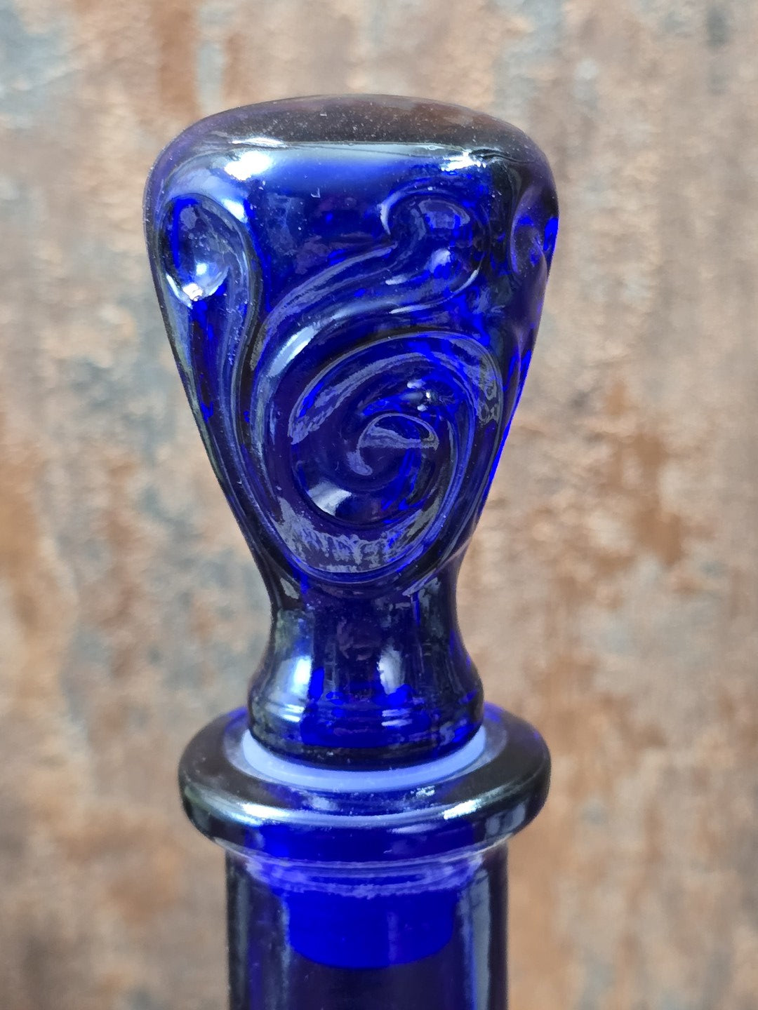 Vintage Glasflakon mit kobaltblauem Glasstopfen, erhabenem Wirbelornament und hellem Dichtungsring in detaillierter Nahaufnahme